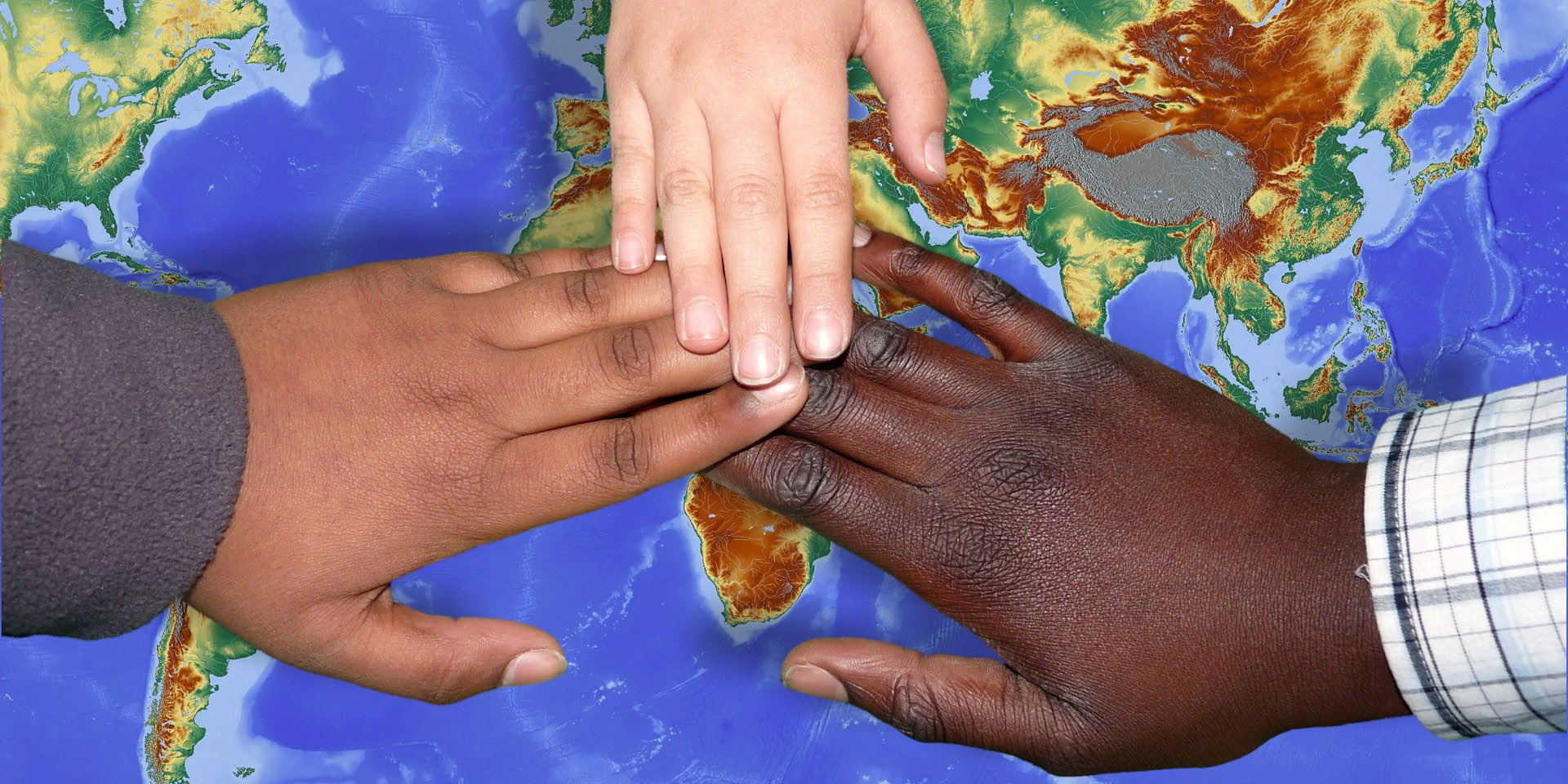 Hände verschiedener Hautfarbe vor der Weltkarte
